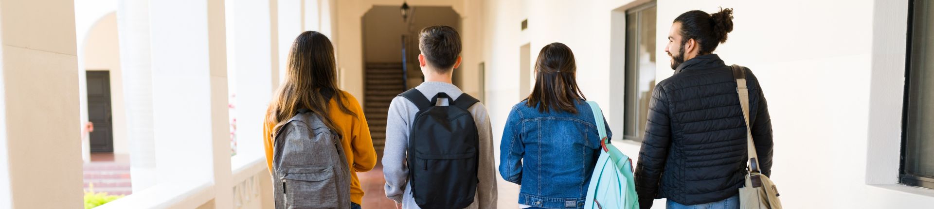 Three college students with backpacks and books on campus stairs outdoors.